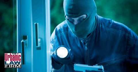 Masked burglar attempting to enter a home with a flashlight and handgun, illustrating Oklahoma burglary crime scenarios defended by the Urbanic Law Firm.
