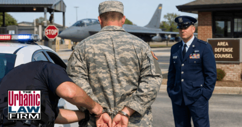 Daytime photo of a uniformed service member in handcuffs beside a police car at an Oklahoma military base while a commanding officer looks on, illustrating serious arrests that can lead to DUI and obscene or threatening communication charges defended by The Urbanic Law Firm’s Oklahoma criminal defense attorneys.