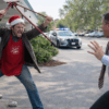 Daytime photo-style image of a Salvation Army bell ringer in a Santa hat lifting a red donation tripod toward a retreating store manager outside a grocery store while police cars approach in the background, illustrating high-stakes Oklahoma criminal defense representation by The Urbanic Law Firm in assault and resisting arrest cases.