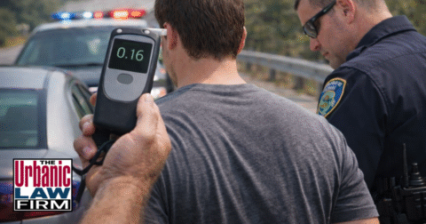 Daytime photo of an Oklahoma police officer standing with a driver on the roadside while a handheld breath tester shows 0.16, illustrating a first-time aggravated DUI Oklahoma traffic stop and the high stakes that call for experienced Oklahoma criminal defense representation by The Urbanic Law Firm.