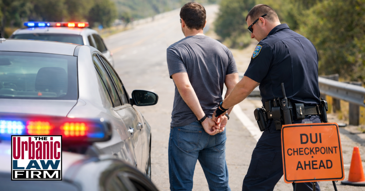 Daytime photo of an Oklahoma police officer handcuffing a driver beside a patrol car at a roadside DUI checkpoint, illustrating Oklahoma aggravated DUI law issues and the serious consequences of DUI stops, with the scene symbolizing the need for strong Oklahoma criminal defense by The Urbanic Law Firm.