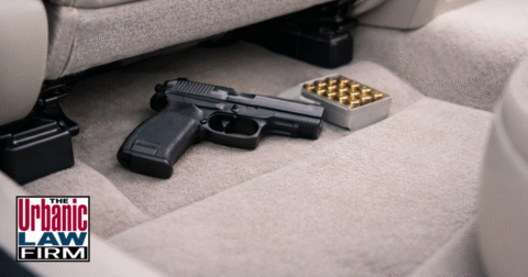 Daytime photograph of a handgun and ammunition on the light floorboard under a car seat, illustrating Oklahoma vehicle firearm offenses and the need for experienced Oklahoma criminal defense representation by The Urbanic Law Firm.