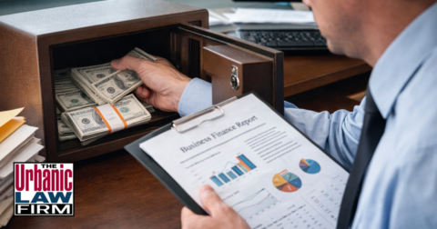 Daytime photograph of a professional secretly taking cash from an open office safe, symbolizing embezzlement crimes in Oklahoma and illustrating experienced Oklahoma criminal defense representation by The Urbanic Law Firm.