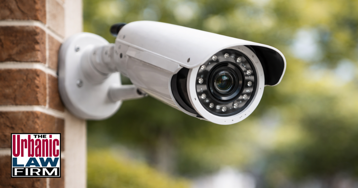 Daytime photograph of a white bullet security camera centered on a brick exterior wall and angled slightly to the right, symbolizing security equipment crimes in Oklahoma and the dedicated criminal-defense representation provided by The Urbanic Law Firm.