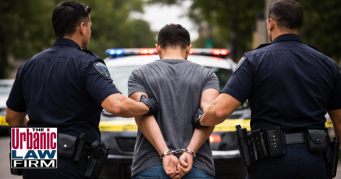 Man in handcuffs escorted by two police officers in daylight for assault on police officer Oklahoma criminal defense content by The Urbanic Law Firm.