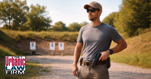 Man standing at an outdoor shooting range in daylight with a holstered handgun, illustrating Oklahoma handgun license issues and Oklahoma criminal defense by The Urbanic Law Firm.