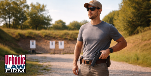 Man standing at an outdoor shooting range in daylight with a holstered handgun, illustrating Oklahoma handgun license issues and Oklahoma criminal defense by The Urbanic Law Firm.