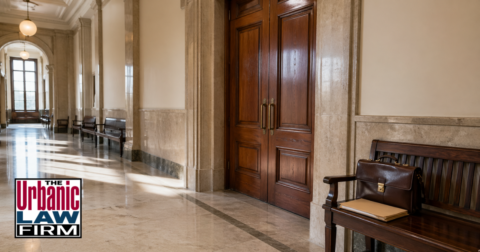 Empty Oklahoma courthouse hallway outside courtroom doors with a leather briefcase and case file on a bench, illustrating Oklahoma indecent exposure criminal defense by The Urbanic Law Firm.