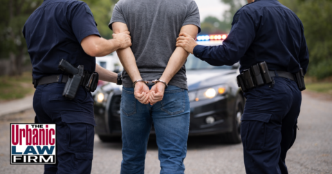 Man being arrested by officers on a roadway in daylight, illustrating Oklahoma police officer maiming charges and Oklahoma criminal defense by The Urbanic Law Firm.