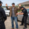 Oklahoma search consent scene showing police frisking a man beside a vehicle outside a home, illustrating Oklahoma criminal defense by The Urbanic Law Firm.