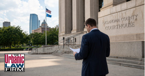 Daytime courthouse scene for self-maiming Oklahoma criminal defense, showing a man reviewing legal documents outside an Oklahoma courthouse, illustrating The Urbanic Law Firm.