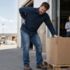 Warehouse worker suffering a workplace retaliation injury after unsafe lifting assignment, with supervisor watching in background, for Cohen & Cohen personal injury lawyers in Alexandria, Virginia.
